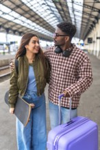 Happy multi ethnic couple walking together on platform while waiting for train, embracing and