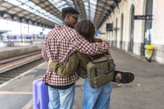 Young couple kissing and hugging on a train station platform, ready for their journey, with luggage