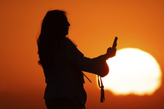 People photographing the sun setting on the horizon with their smartphones from the summit of the
