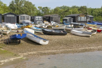 Dinghies on beach with black fishing sheds and Riverside Tearoom cafe, Orford, Suffolk, England, UK