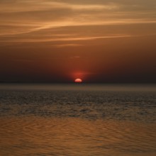 Atmospheric sunset... Cuxhaven, North Sea, in calm weather, glowing red sun sinking into the sea,