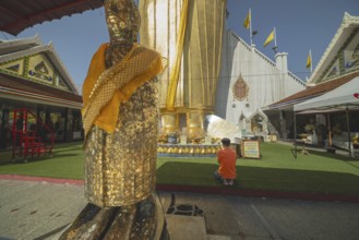 Man praying in front of a 32 metre high standing Buddha decorated with glass mosaics and 24 carat
