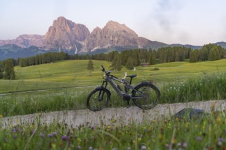 A bicycle stands on a gravel road with a view of the nearby Dolomites, Sassolungo Group, Alpe di