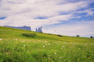 Wide meadow with cross and cable car in the background under a blue sky, Alpe di Siusi, Dolomites,