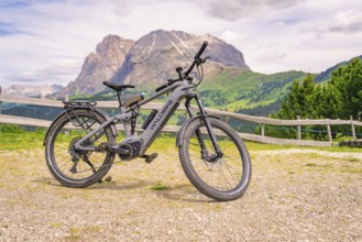 Grey e-bike on a stony path with mountain view and wooden fence in the background, Alpe di Siusi,