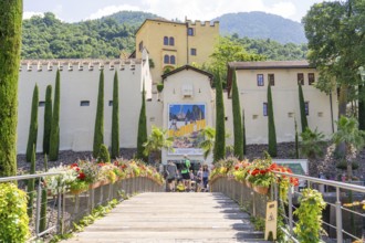 A bridge with flowers leads to colourful buildings in front of a mountainous landscape, Botanical