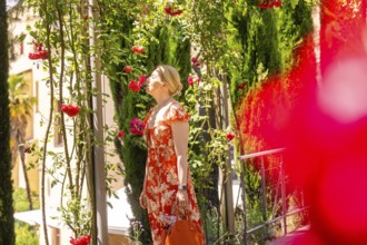 Woman in red dress smelling flowers on a plant path, surrounded by summer light, Botanical Garden,