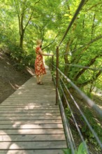 A woman on a wooden footbridge in the forest, surrounded by green trees, Botanical Garden, The