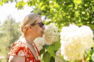 Woman in a red dress smelling a white flower, surrounded by green plants, Botanical Garden, The