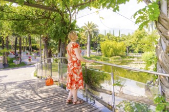 Woman in floral dress enjoying the view of a park-like pond, Botanical Gardens, The Gardens of