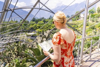 Woman in a red summer dress looking at a map in front of a glass construction, Botanical Garden,