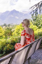 Woman in a red dress sitting on a bench and enjoying the view of the mountains, Botanical Garden,