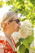 Woman smelling a white flower, surrounded by green plants, wearing a red dress, Botanical Garden,