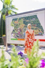 Woman in orange dress looking at a large map in a garden, Botanical Garden, The Gardens of