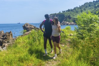 Interracial couple walking along a coastal path, enjoying the scenic views of the ocean and green