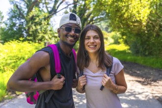 Hikers wearing backpacks are smiling joyfully while trekking along a forest path, enjoying the