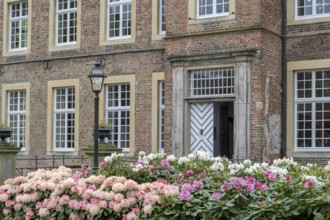 Brick building with large entrance door, blooming rhododendrons and an old lantern in the