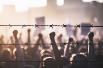 Barbed wire barrier with blurred protest crowd. A poignant image of resistance and struggle at