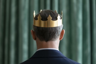 Man in suit wearing golden crown seen from behind. Formal portrait evokes themes of monarchy,