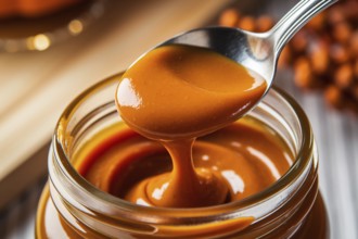Close-up of silver spoon scooping rich pumpkin butter from glass jar. Warm autumn kitchen scene