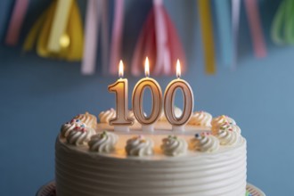 Close up of 100th birthday cake with flickering candle. Celebration of longevity and reaching a