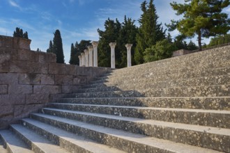 Stone staircase with old columns, framed by trees under a blue sky, open staircase to the second