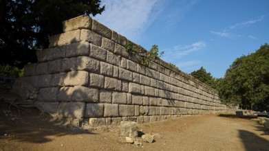 Stone wall in a natural setting with clear blue sky, Wall Upper Terrace, Asklipion, Asklepieion,