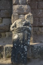 Damaged stone statue in antique garment in front of an old stone wall, antique statue of gods,
