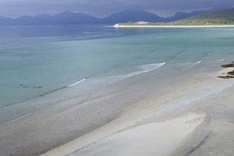 Gentle waves lap the wide, empty beach against a backdrop of mountains and a calm sea, Seilebost