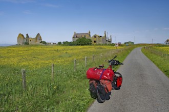 Luggage-laden bike on road next to flowering fields and ruins under clear sky, cycle tour, South