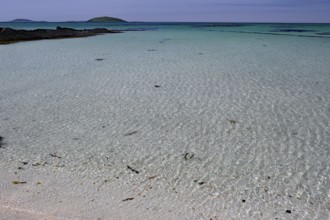 Crystal clear turquoise water on a sandy beach with islands on the horizon under a blue sky,