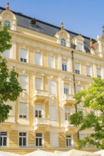 Historic building with yellow façade and balconies against a blue sky, Merano, Italy