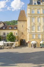 Historic square with a medieval tower and surrounding buildings, illuminated by the warm summer