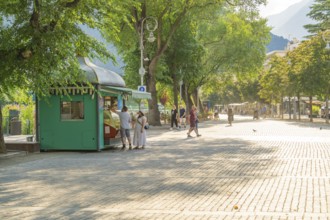 People walking on a sunny promenade with an ice cream shop in the foreground, Merano, Italy