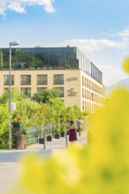 Modern hotel building with green surroundings and walkers against a mountain backdrop, Merano,