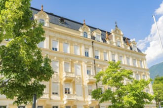Classic building with elegant façade flanked by green trees under a blue sky on a sunny day,
