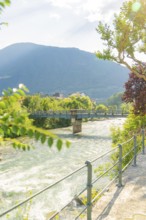 River with bridge, surrounded by green nature and mountains in sunlight, Merano, Italy