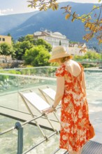 Woman in summer dress looking at view from a bridge with river and mountains, Merano, Italy