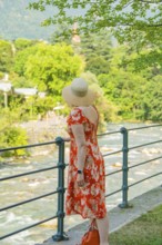 A woman in a flowered dress looks at a flowing river on a sunny day, Merano, Italy