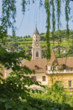 Church tower and building surrounded by green trees and hills, Merano, Italy