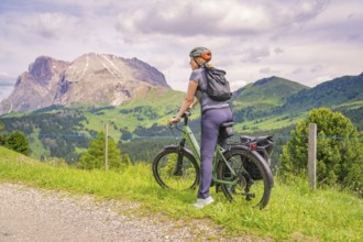 Cyclist on a path with a view of a mountain landscape under a cloudy sky, Alpe di Siusi, Dolomites,