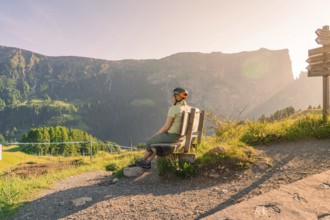 Person with bicycle helmet on a bench on a hiking trail with a view of imposing mountains, Alpe di
