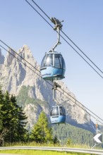 Blue cable car gondolas in front of a rocky mountain backdrop in fine weather, Alpe di Siusi,