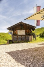 Wooden hut as an ice cream stand in a meadow in the mountains in the sunshine with flags and