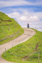 A cyclist rides on a winding hilly path in sunny weather, Alpe di Siusi, Dolomites, South Tyrol,