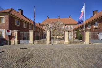 Cathedral administration, brick building, tree, cobblestone pavement, flags on flagpoles, blue