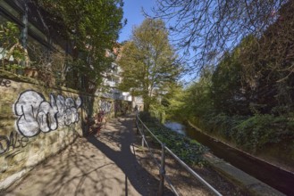 Footpath, sandstone wall, graffiti, metal railing, river Münstersche Aa, trees, bushes, shadow,