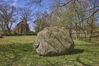 Boulder from southern Sweden, granite, Saale Ice Age, lawn, bare winter trees, blue cloudless sky,