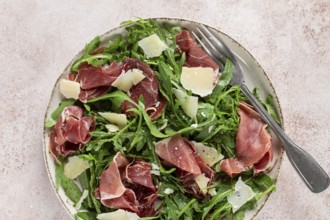 Fresh arugula salad with prosciutto and grated parmesan cheese, on a plate, homemade, no people