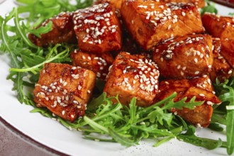 Fried salmon slices, teriyaki with sesame seeds, with arugula salad, top view